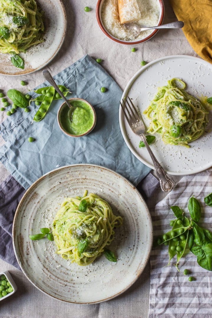 pea pasta made with spaghetti and a basil and pea pesto served up on 3 plates with extra parmesan and pesto at the side