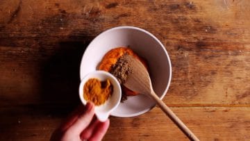 1 teaspoon curry powder being added to bowl containing 3 tablespoon of thai red paste and half teaspoon of ground coriander