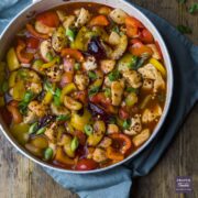 Sweet and sour chicken in a large pan topped with spring onions and chilli flakes.