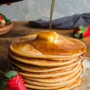 A stack of American pancakes with a piece of butter melting on the top and syrup poured over and drizzling down one side.