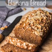 Banana bread loaf on brown crumpled paper with 2 pieces sliced and falling down from the front of the loaf.