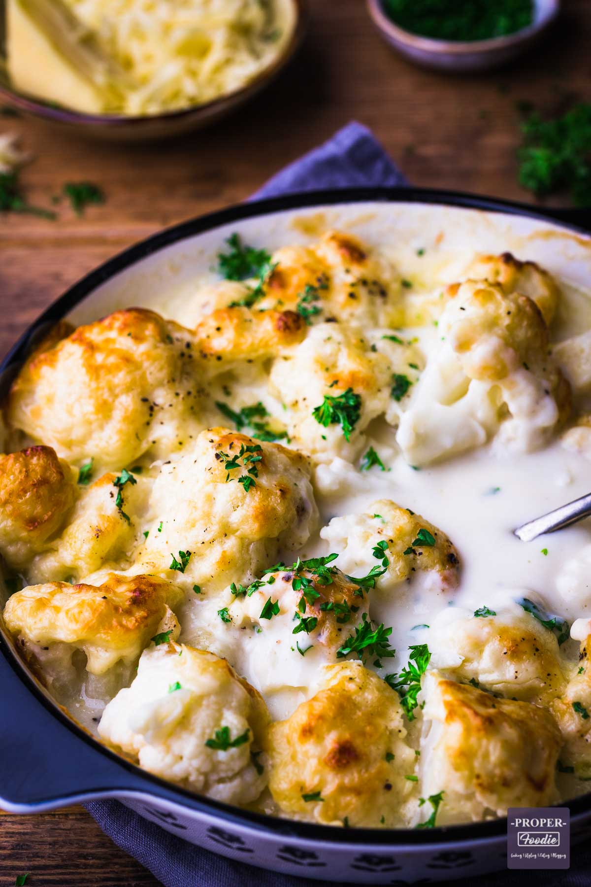 Cauliflower in a creamy cheese sauce presented in a shallow dish and topped with baked on cheese and parsley