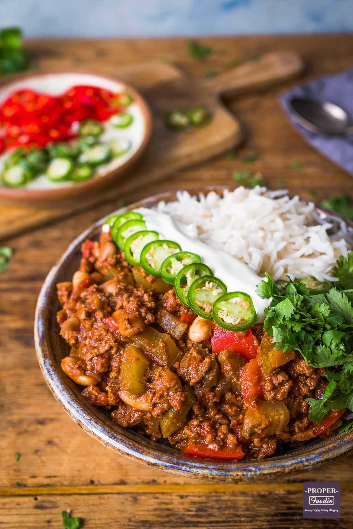 chilli con carne in a bowl with rice, green chillies, soured cream and fresh coriander