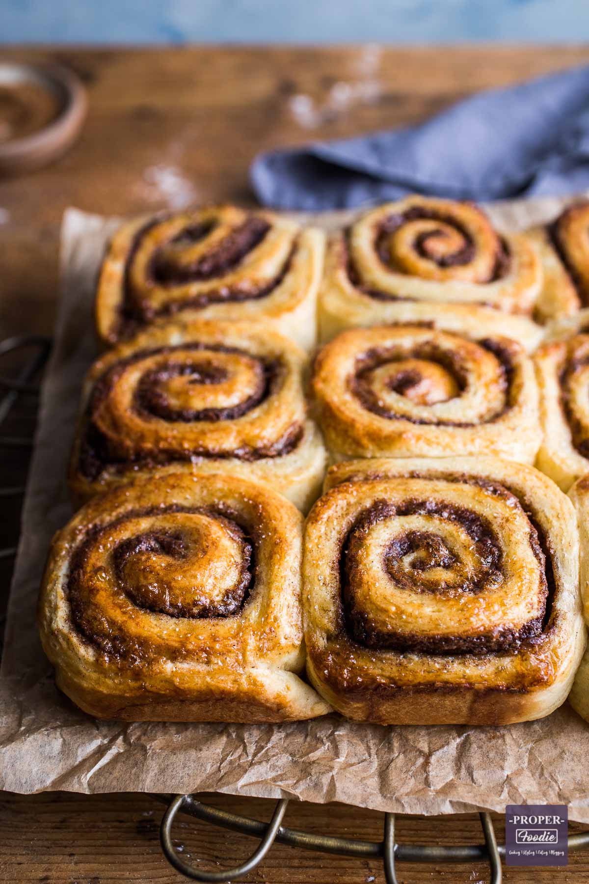 Baked cinnamon swirls stuck together in two side by side rows of three. Golden brown and lying on top of brown paper.