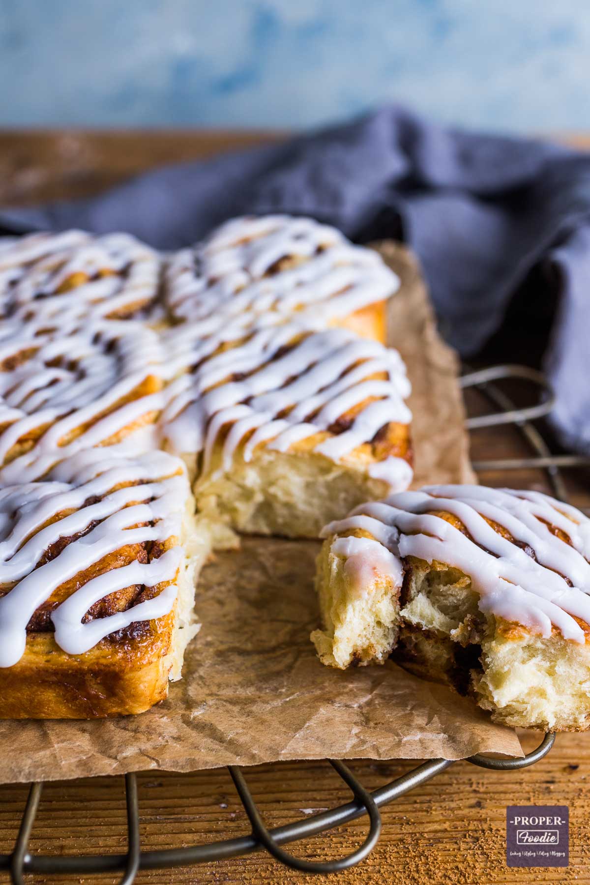 Baked cinnamon swirls stuck together in two side by side rows with icing on the top and one roll broken off with a bite taken.