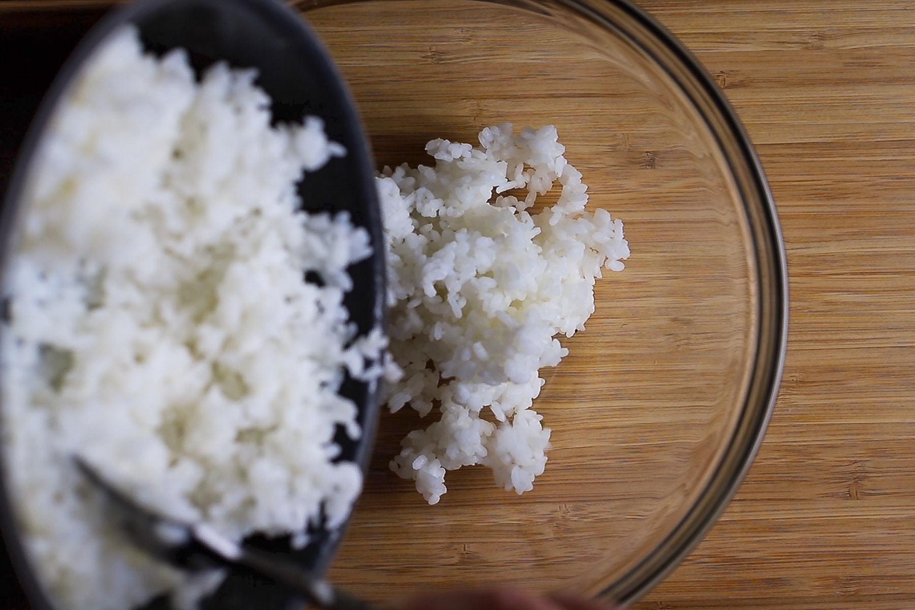 cooked rice being transferred from a pan into a mixing bowl