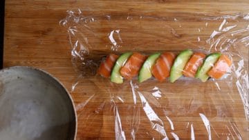 cover dragon roll with cling film to shape and press the topping to the roll