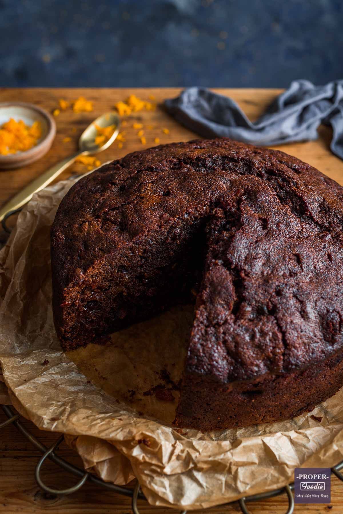 Fruit Christmas cake without icing sitting on brown paper, on a bronze cooling rack, with a slice taken