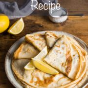 Plate of thin, flat English pancakes with the top 4 folded into quarters ad 2 lemon wedges placed on top.