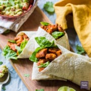 three healthy paprika chicken wraps on a board with a bowl of guacamole in the background