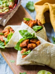 three healthy paprika chicken wraps on a board with a bowl of guacamole in the background