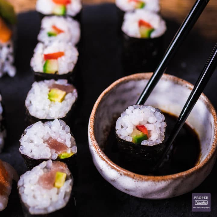 maki sushi on a platter with one piece being dipped in soy sauce with chop sticks