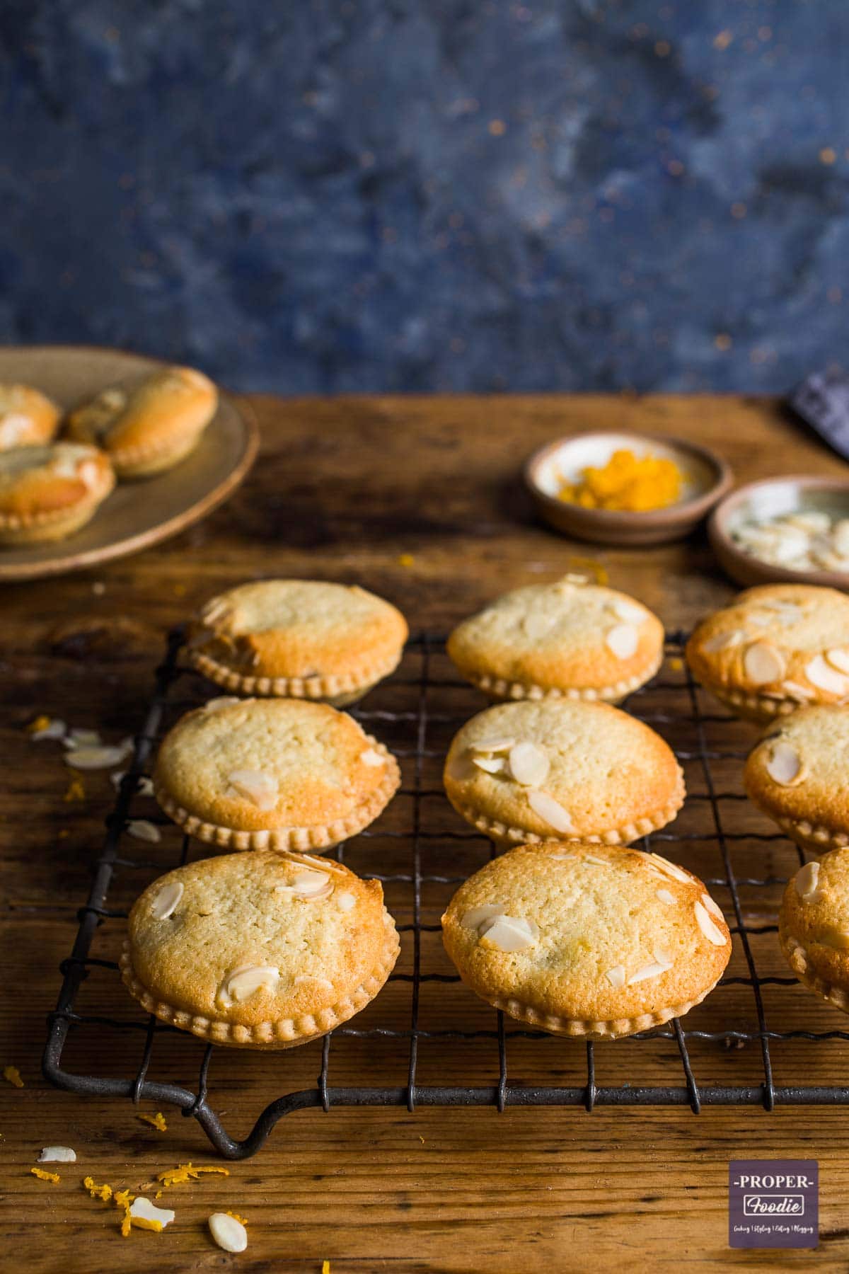 Frangipane mince pies lined up on a wire cooling rack with more pies in background on a plate.