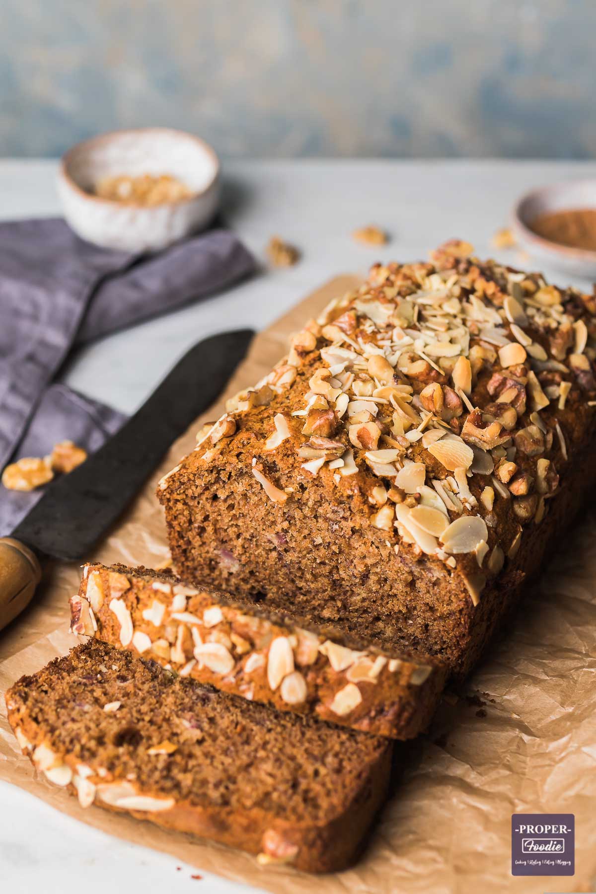 Banana bread loaf on brown crumpled paper with 2 pieces sliced and falling down from the front of the loaf.