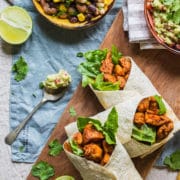 three healthy chicken wraps on a board with a spoonful of guacamole next to them and the edge of a bowl of mixed bean salad just visible