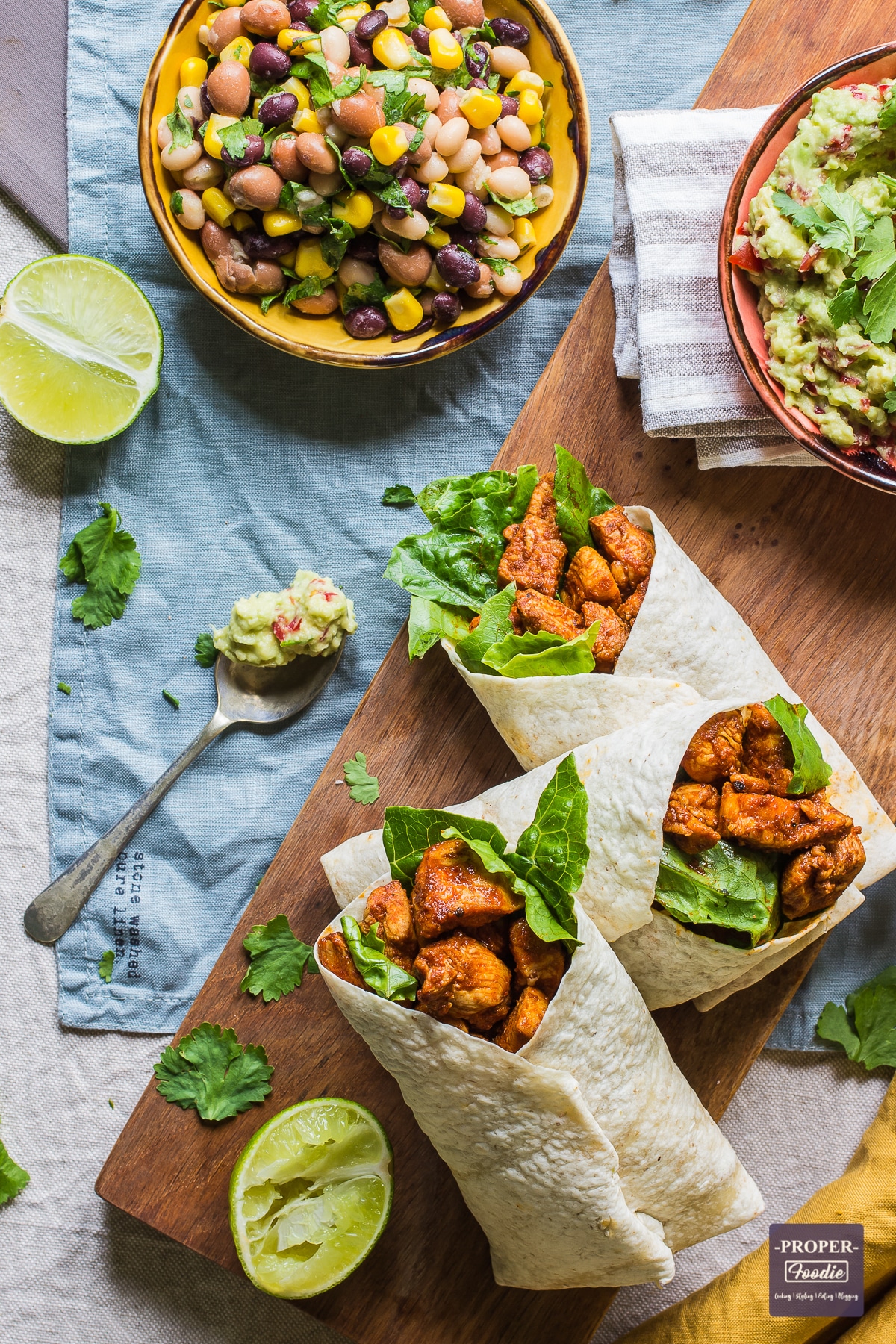 three wraps with paprika chicken and a spoonful of guacamole next to them and the edge of a bowl of mixed bean salad just visible