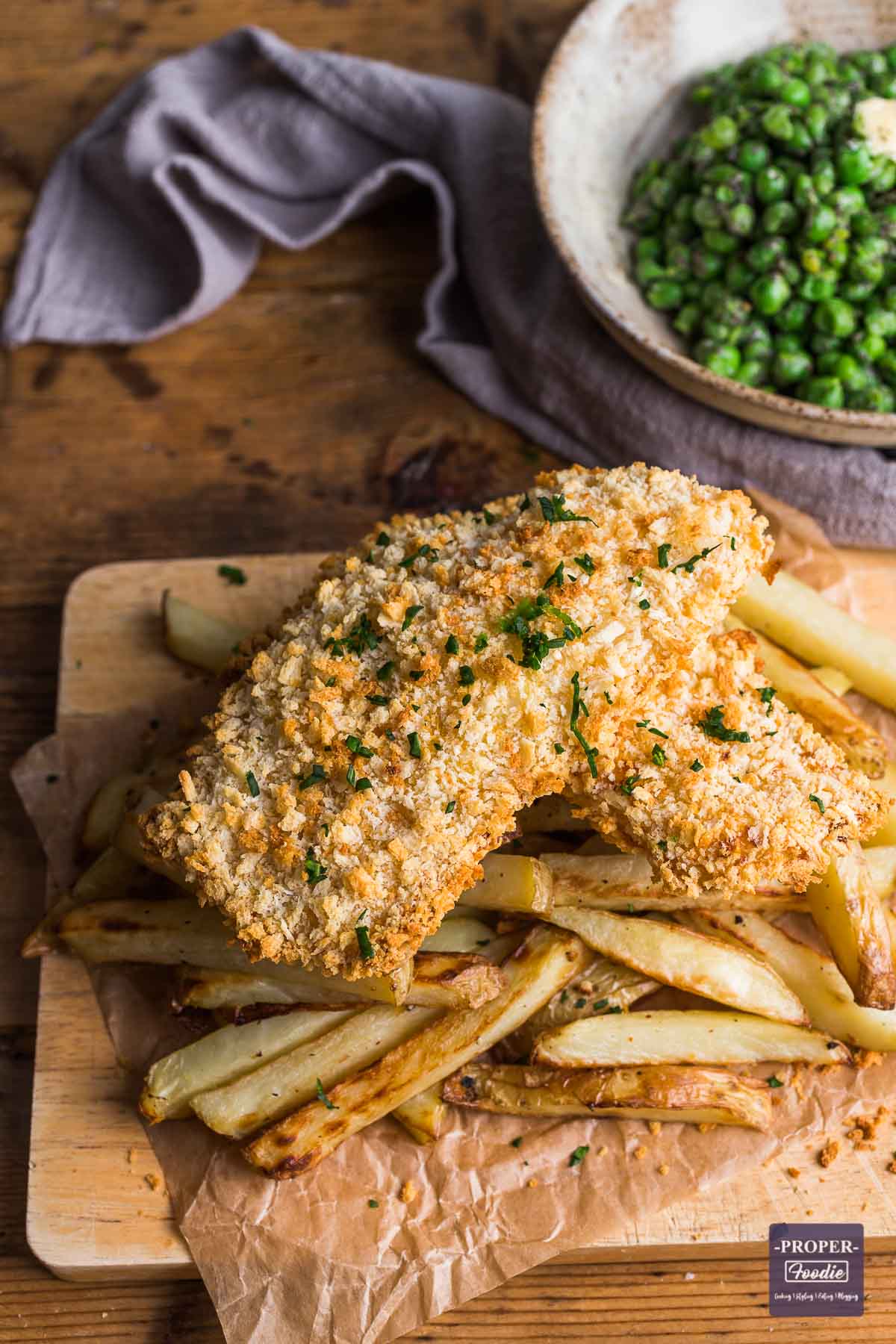 Two fillets of fish in golden bread crumbs sat on a pile of homemade oven chips