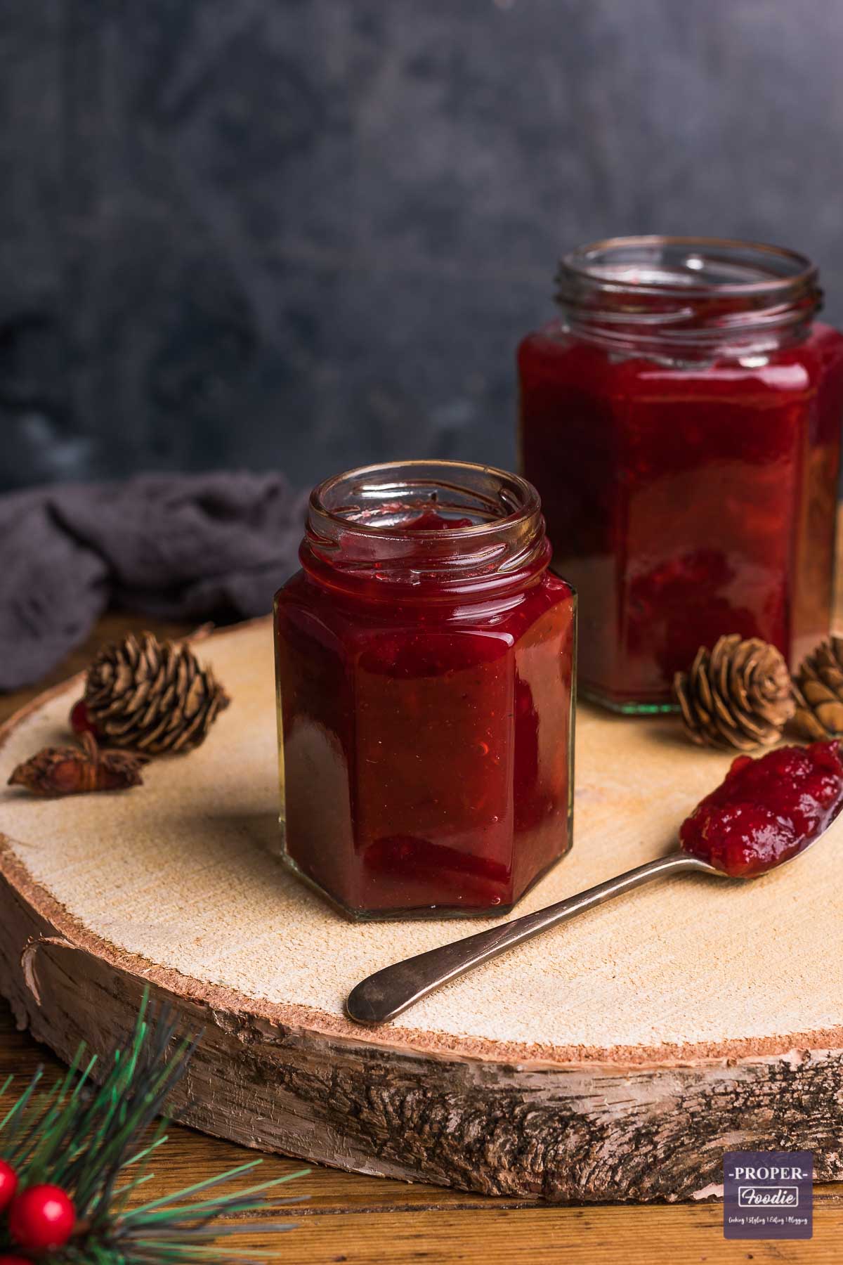 Homemade cranberry sauce in a small jar with a teaspoonful of sauce at the side with larger jar in background.