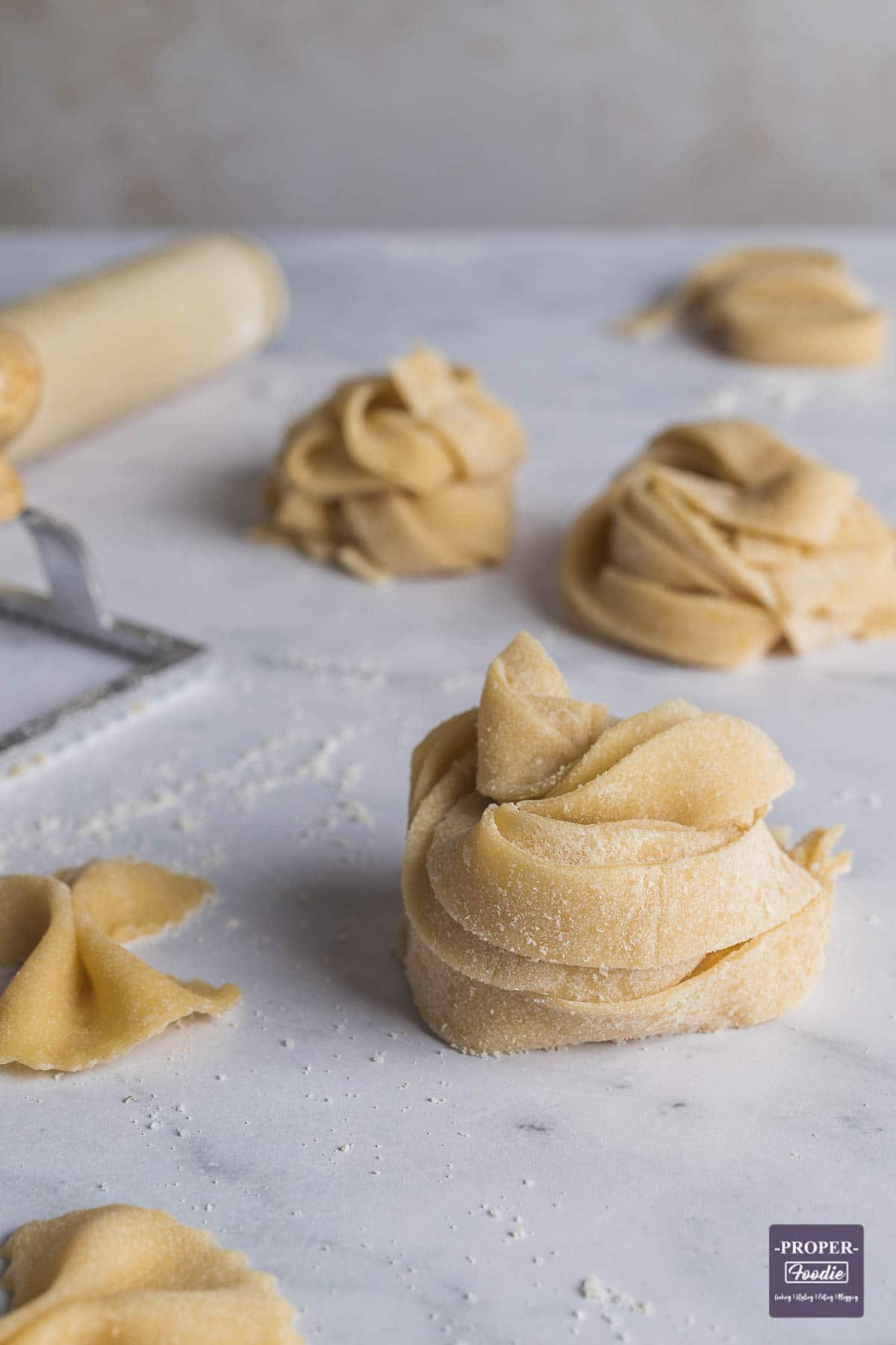 Strips of fresh pasta wrapped into a nest and sprinkled with semolina and further nests in background.