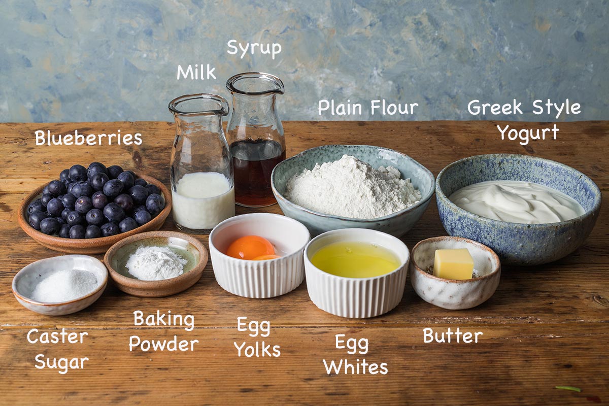 A display of the ingredients needed to make Blueberry American style pancakes with text overlay stating each ingredients