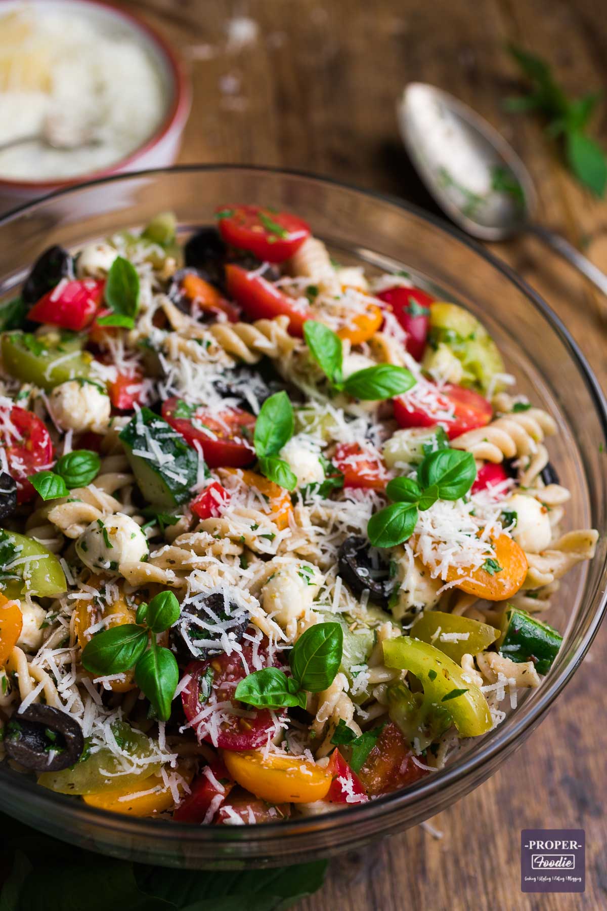 Large bowl filled with Italian Pasta Salad with a serving spoon and small bowl of grated pecorino cheese in the background.