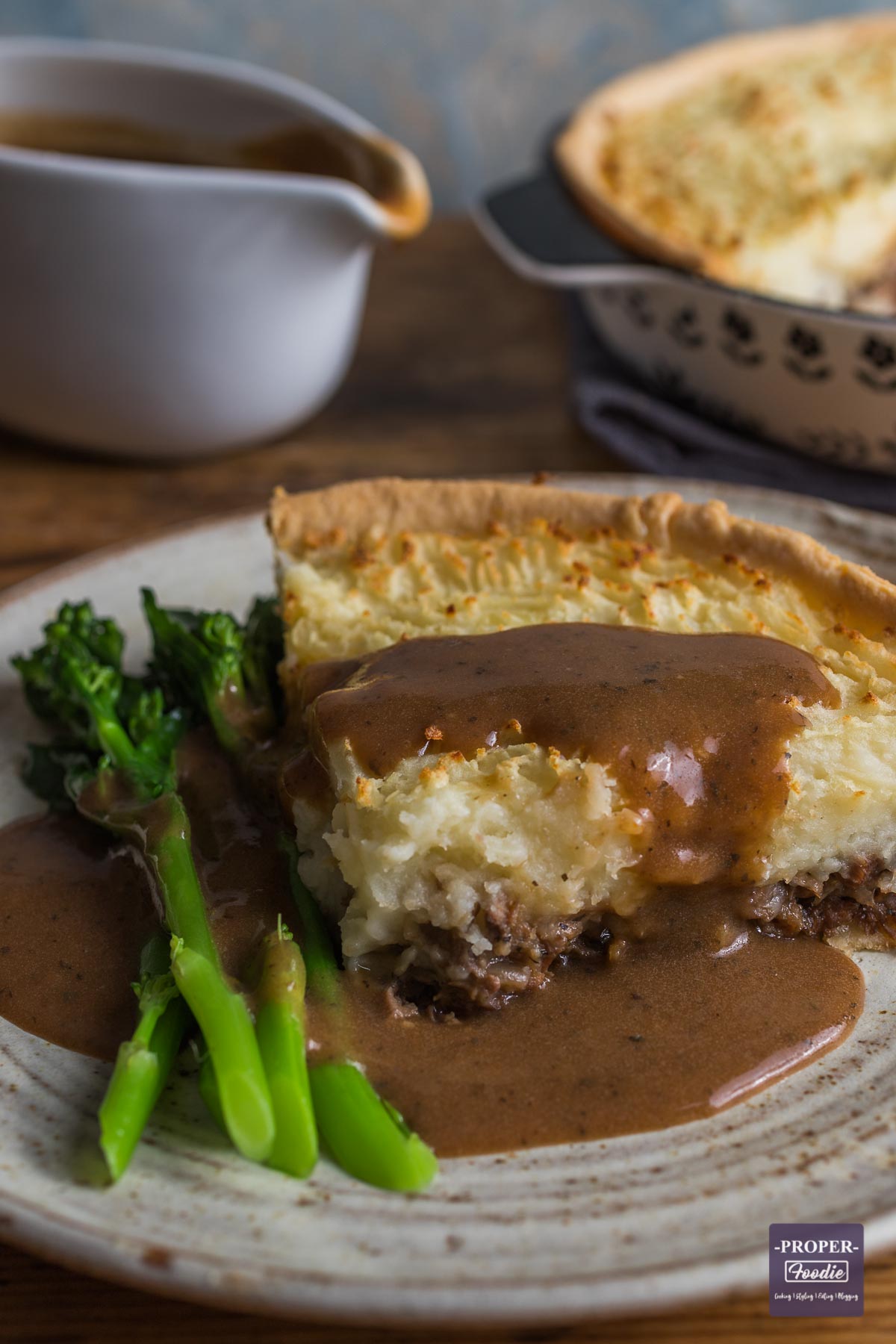 Slice of lamb pie with mash topping and pastry bottom, served with mint gravy poured over the top.