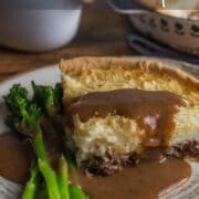 Slice of lamb pie with mash topping and pastry bottom, served with mint gravy poured over the top.