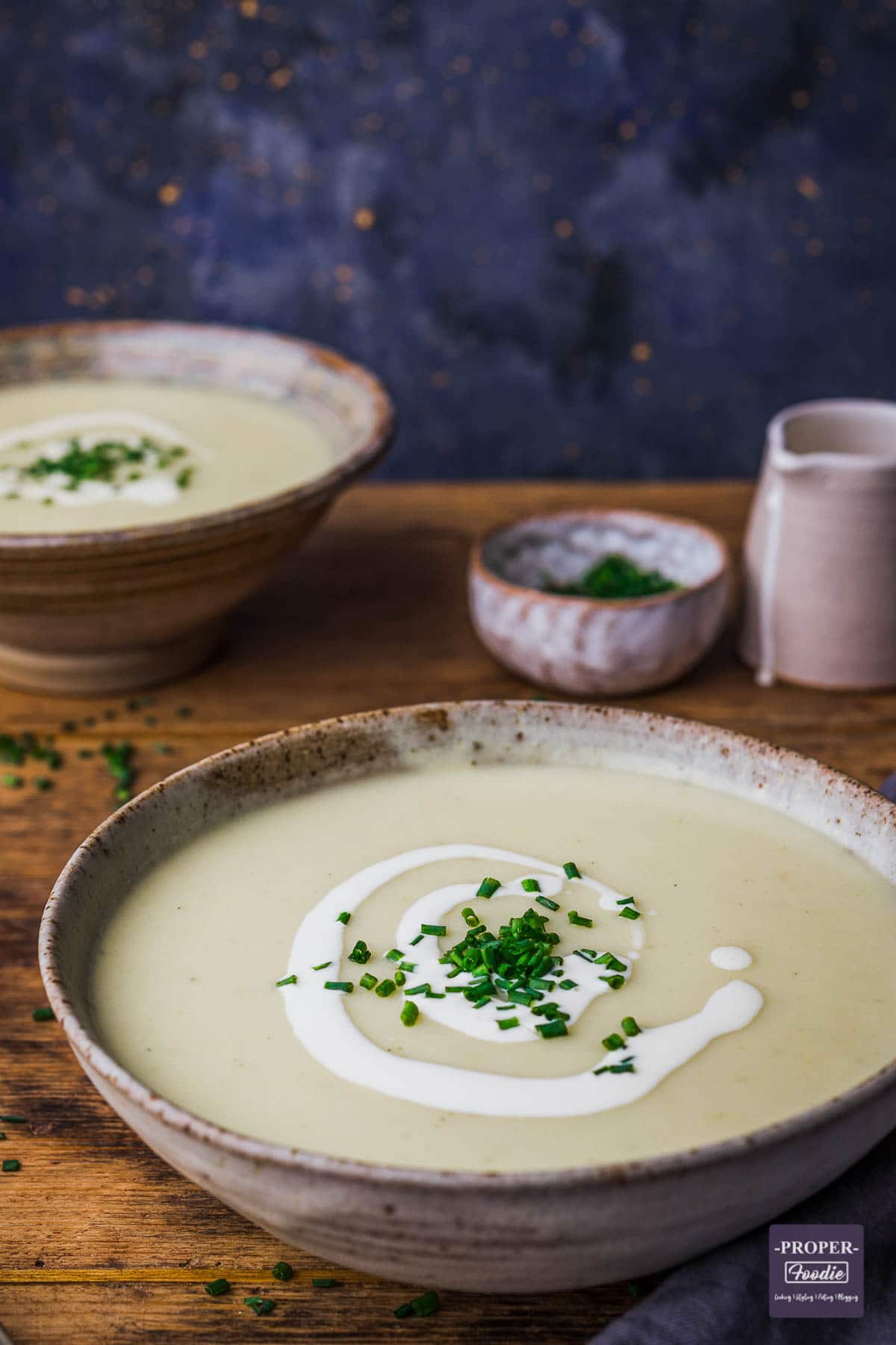 A bowl of leek and potato soup topped with a swirl of cream and chopped chives.