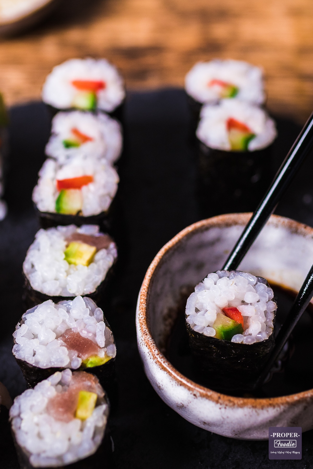 maki sushi on black slate with one piece being dipped in soy sauce