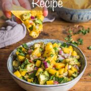 Bowl of mango salsa with some being scooped out on a tortilla crisp.