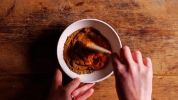 mixing together thai red paste with coriander, curry powder, cumin and black pepper to make thai yellow paste