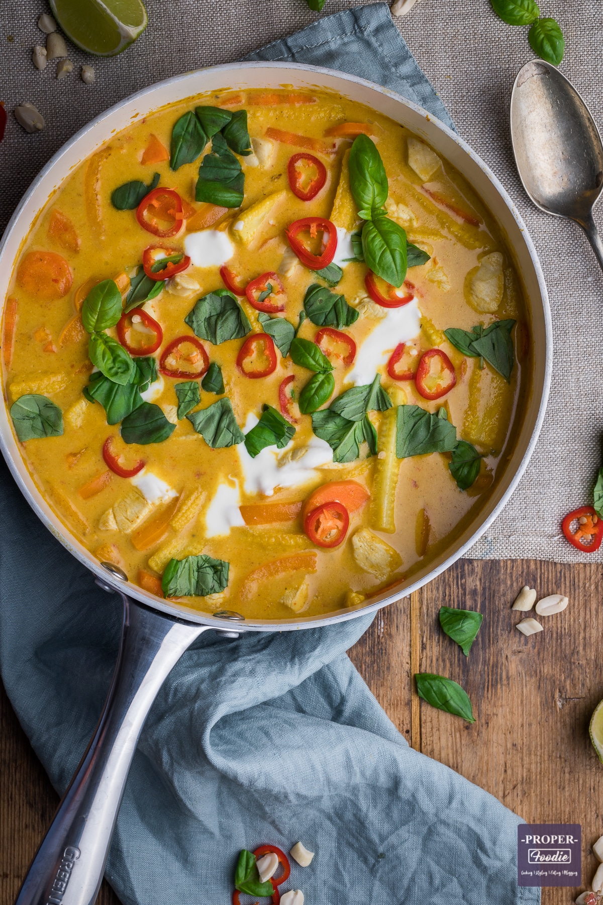 Chicken panang curry in a large pan and topped with yogurt, fresh red chillies and fresh basil leaves