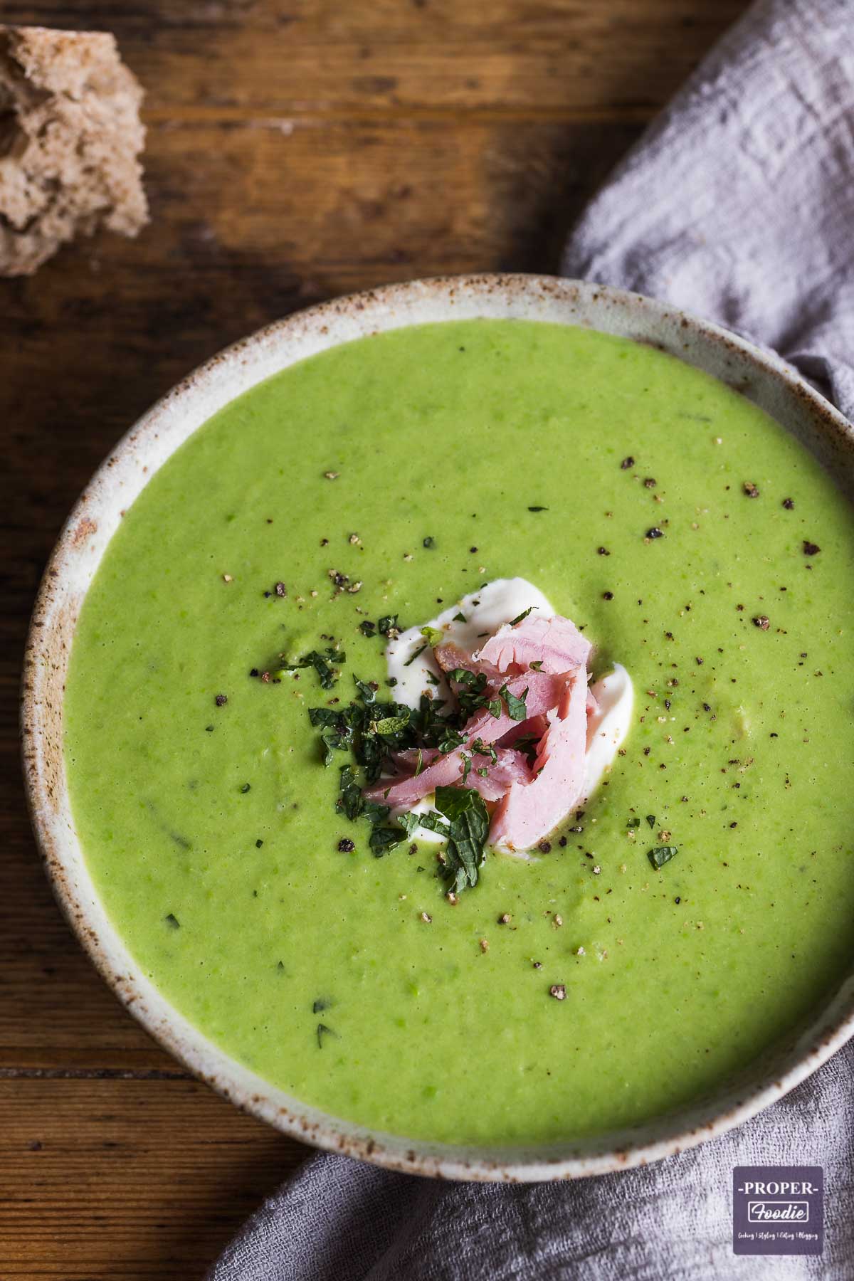 Pea and ham soup in a bowl topped with creme fraiche, chunks of ham and fresh mint