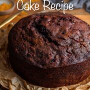 Fruit Christmas cake without icing sitting on brown paper, on a bronze cooling rack, with orange zest and a gold spoon in background.