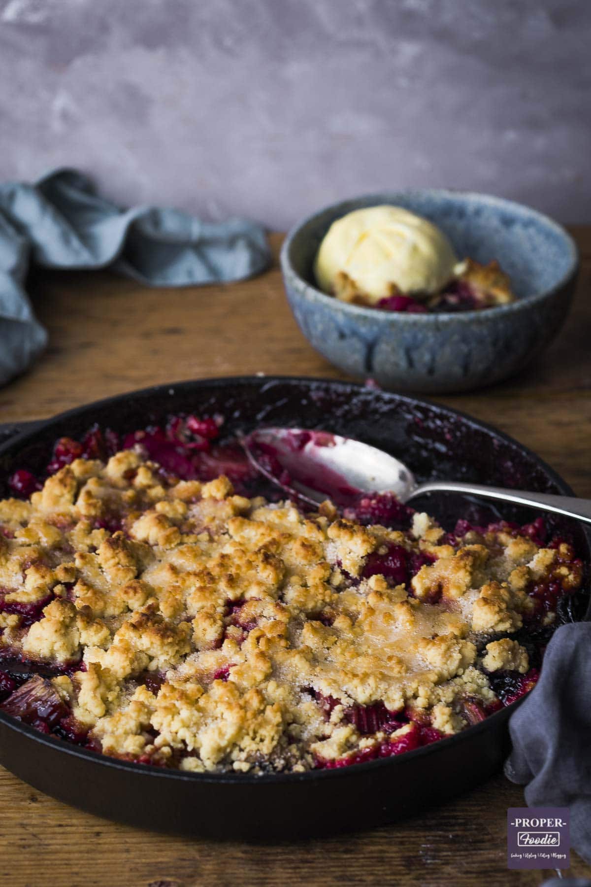 Plum and rhubarb crumble baked in a iron pan with some served in a bowl with ice cream.