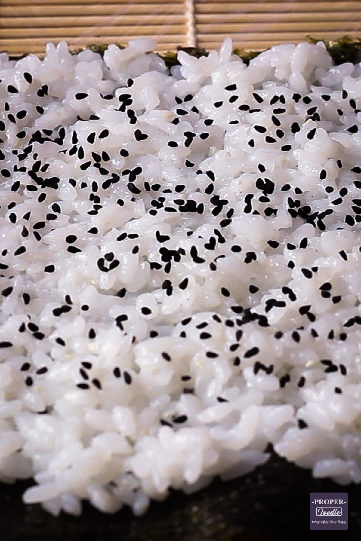 Sushi rice spread onto a nori sheet with black sesame seeds sprinkled on top