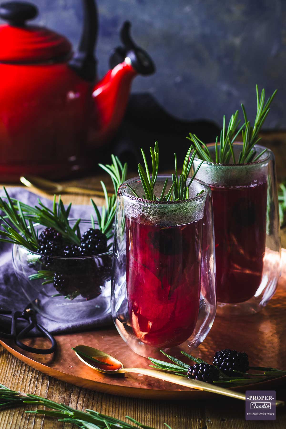 Two double wall tall glass filled with purple berry hot toddy and decorated with sprigs of rosemary.