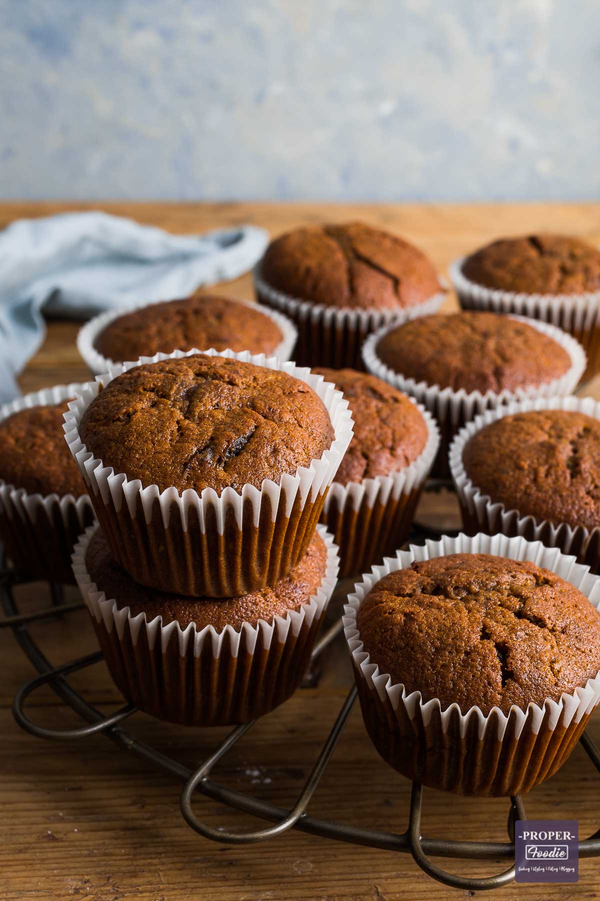 Pumpkin muffins on a round, bronze cooling rack with two of the muffins stacked one on top of the other.