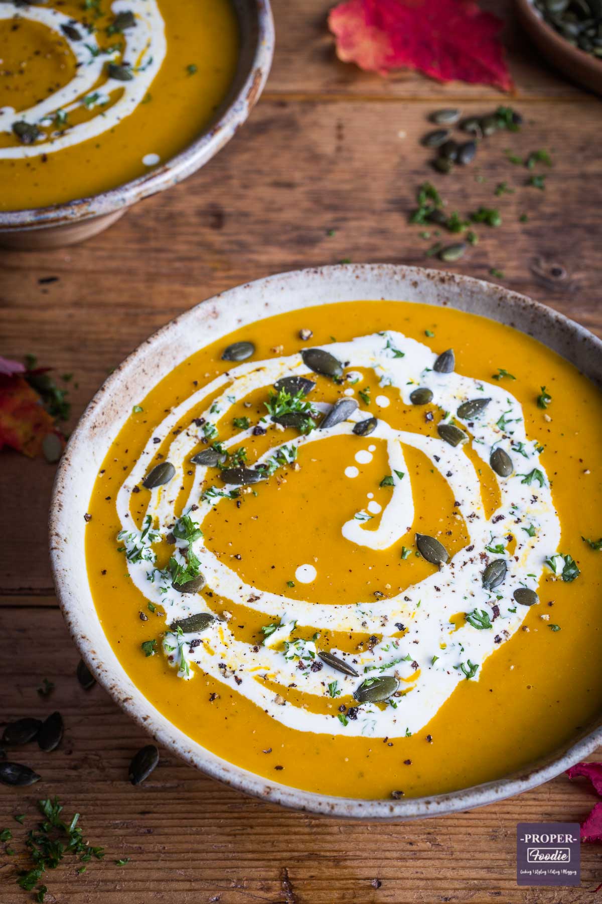 Bowl of pumpkin soup topped with a swirl of cream and a second bowl of soup in the background