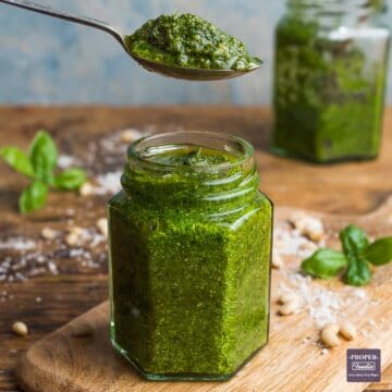 Homemade basil pesto in an open jar with a teaspoon of pesto held above the jar.