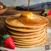 A stack of American pancakes with a piece of butter melting on the top and syrup poured over and drizzling down one side.