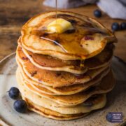 Stack of American style blueberry pancakes with a piece of butter on top and syrup being poured over