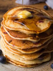 Stack of American style blueberry pancakes with a piece of butter on top and syrup being poured over