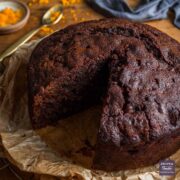 Fruit Christmas cake without icing sitting on brown paper, on a bronze cooling rack, with a slice taken