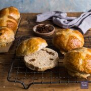 hot cross buns on a cooling rack with one sliced in half