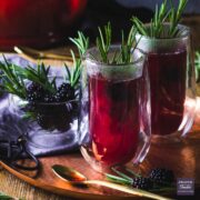 purple and steaming sloe gin hot toddy served in 2 double wall glasses, with sprigs of rosemary and on a bronze tray.