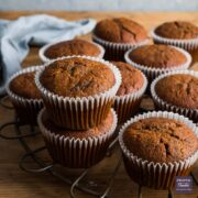 Pumpkin muffins on a round, bronze cooling rack with two of the muffins stacked one on top of the other.