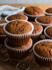 Pumpkin muffins on a round, bronze cooling rack with two of the muffins stacked one on top of the other.