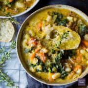 A Tuscan vegetable and bean soup served up in two bowls and topped with crusty bread, grated parmesan and fresh sprigs of thyme.