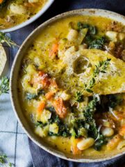 A Tuscan vegetable and bean soup served up in two bowls and topped with crusty bread, grated parmesan and fresh sprigs of thyme.